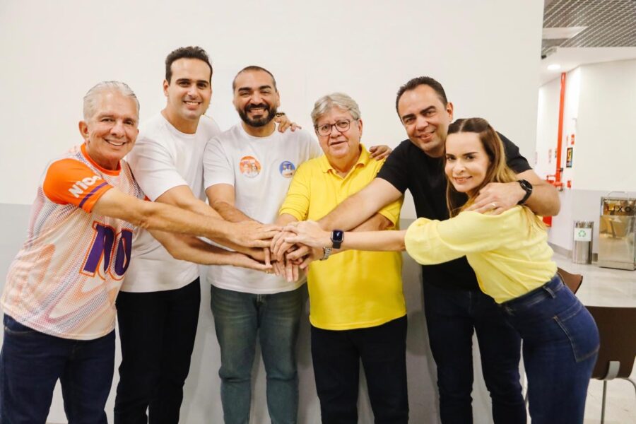 Nabor Wanderley, Lucas Ribeiro, o prefeito Jan de Manoel da Lenha, João Azevêdo, aliado político e a senadora Daniella Ribeiro unem as mãos sobrepostas ao centro em ambiente interno.