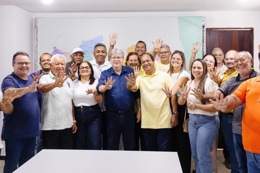 João Azevêdo posa sorridente cercado por grupo de apoiadores de Lucena, com um homem de camisa laranja ao lado