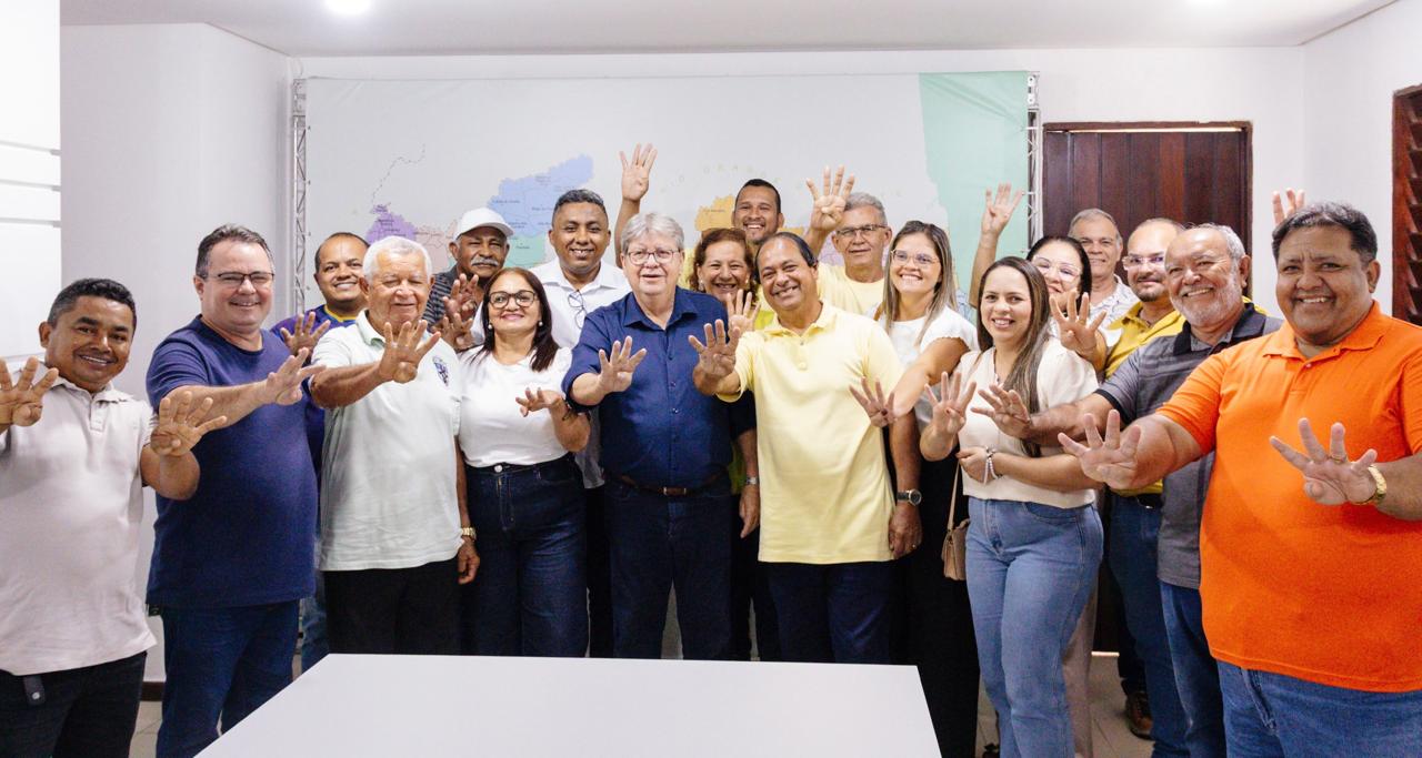 João Azevêdo posa sorridente cercado por grupo de apoiadores de Lucena, com um homem de camisa laranja ao lado