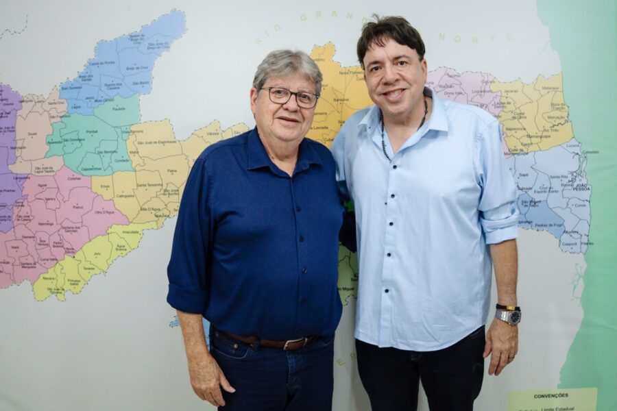 João Azevêdo e o vereador Guguinha Moov Jampa posam lado a lado sorrindo em frente a um mapa da Paraíba