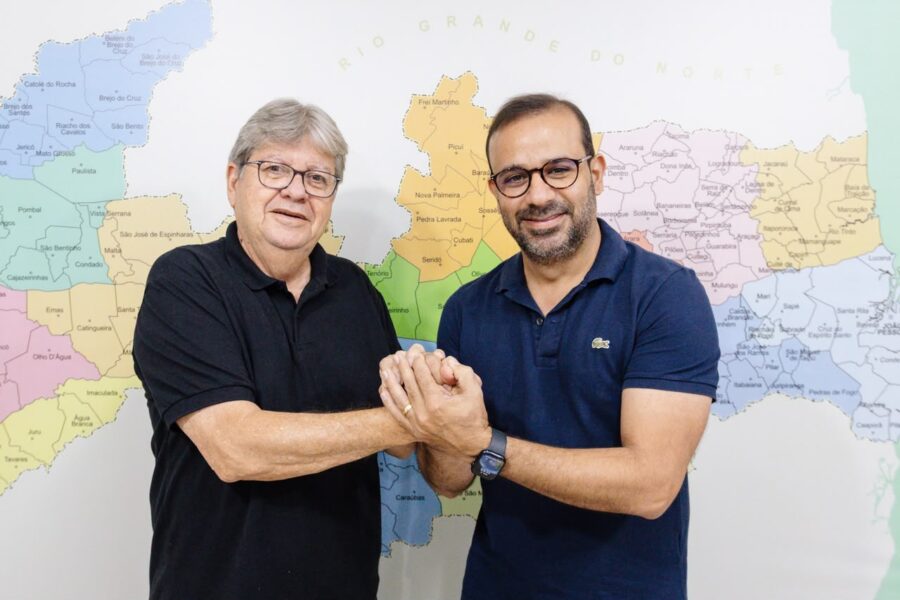 João Azevêdo e o prefeito de Santa Luzia, Henry Lira, posam sorrindo de mãos dadas em frente a um mapa da Paraíba