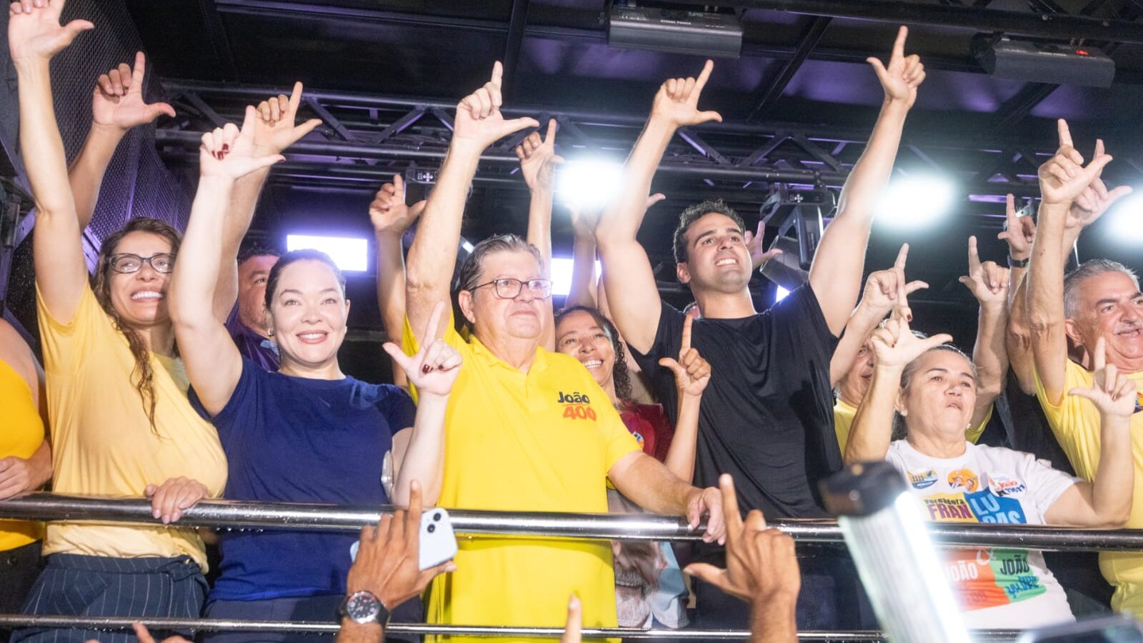Lucas Ribeiro, João Azevêdo e apoiadores comemoram em cima de veículo com mãos levantadas fazendo gesto de campanha