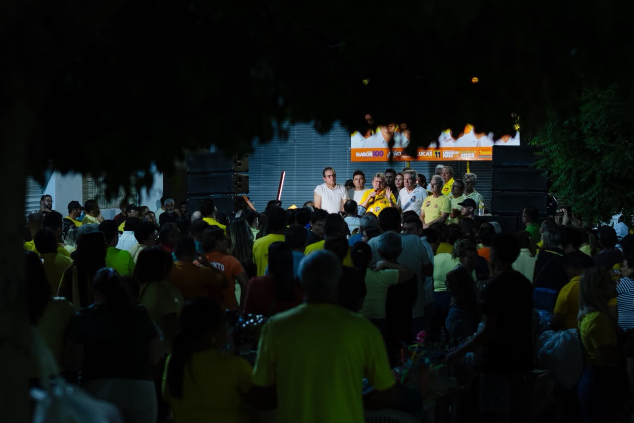 Visão geral noturna de comício em Sousa com João Azevêdo no palco cercado por lideranças e grande público.