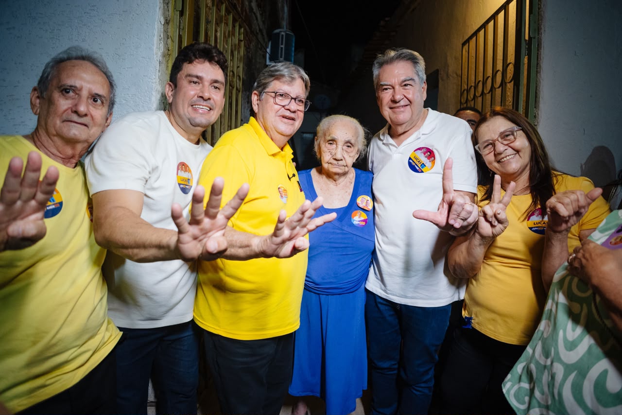 João Azevêdo sorri ao lado de idosa vestindo azul, acompanhado de Helder Carvalho e Lindolfo Pires.