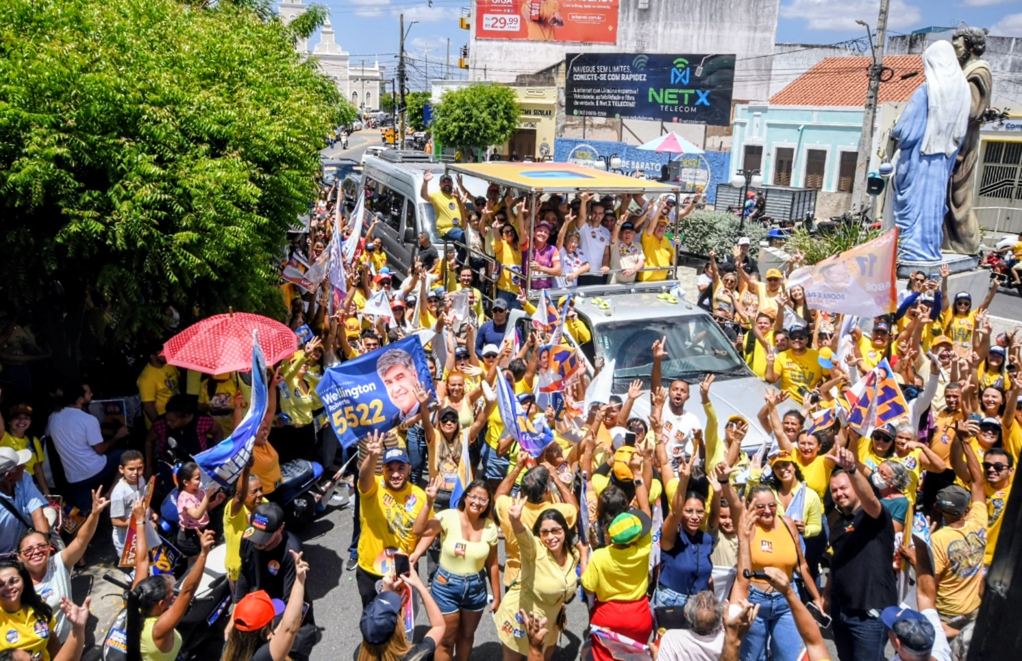 Vista superior de carro aberto com a comitiva cercado por apoiadores com bandeiras e sombrinha vermelha em Uiraúna.