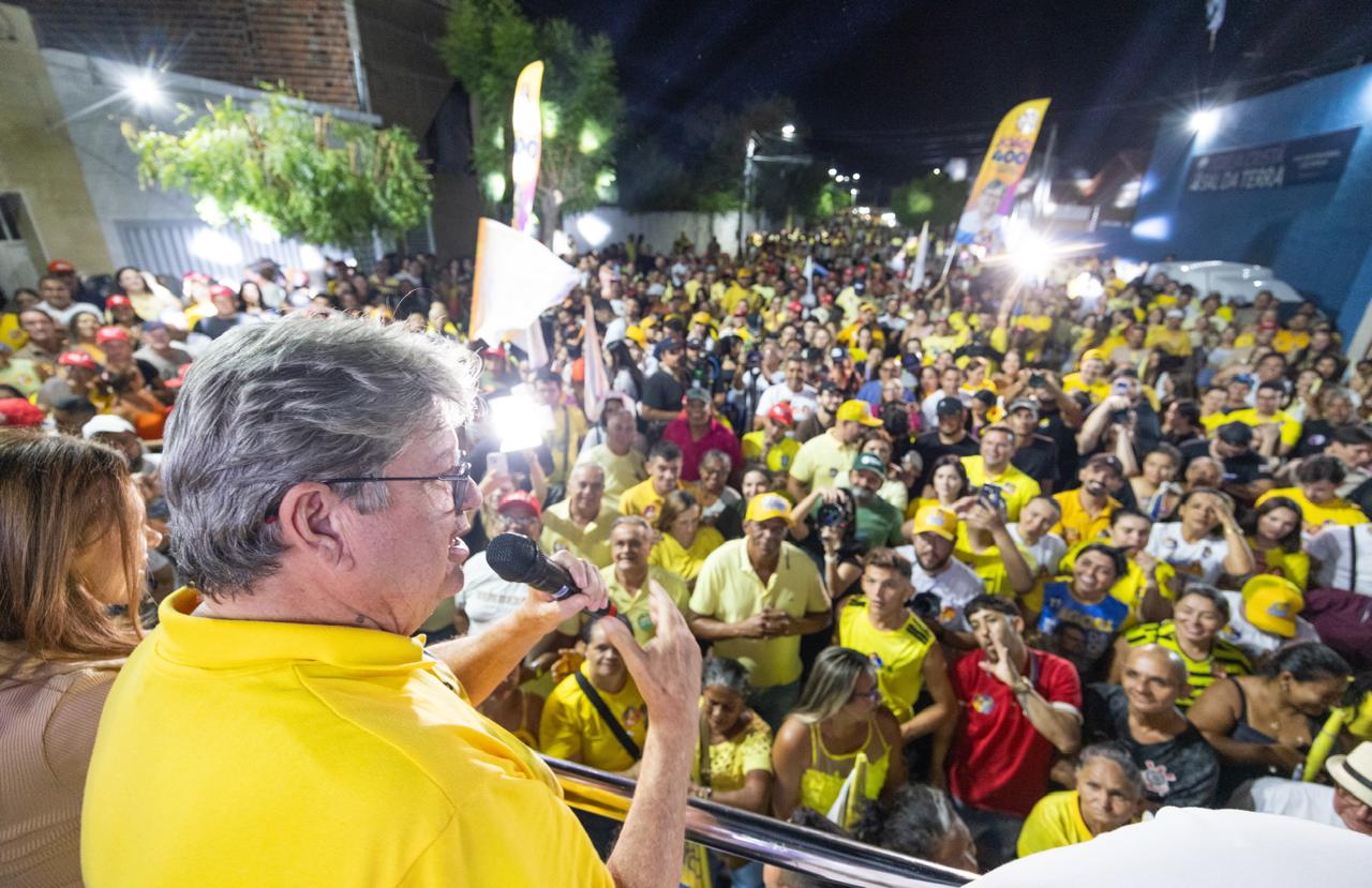 João Azevêdo de camisa polo amarela discursa ao microfone diante de grande público nas ruas de Cajazeiras.