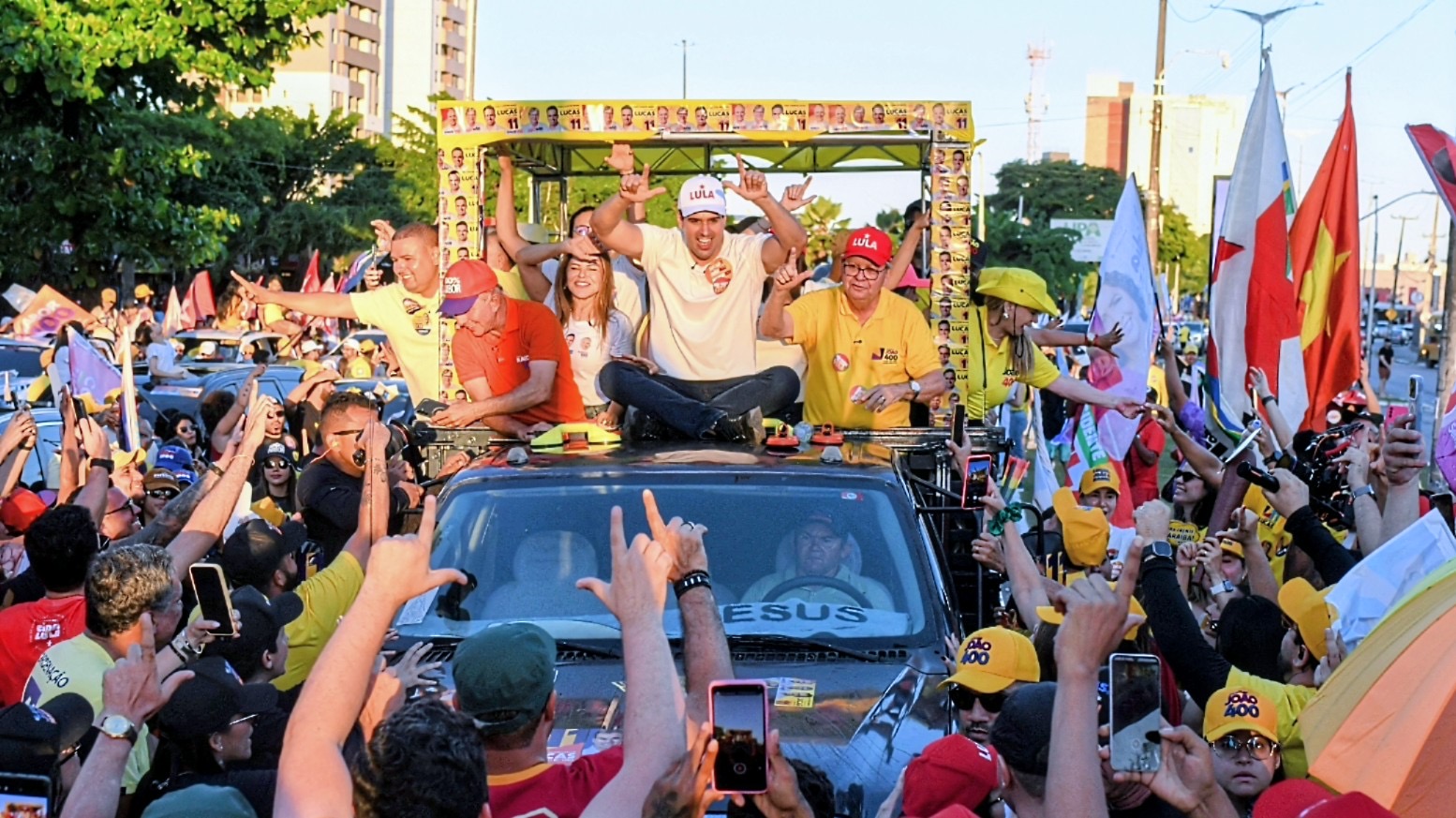 Multidão faz sinal de vitória e campanha com as mãos em direção a João Azevêdo e Lucas Ribeiro sobre o veículo.