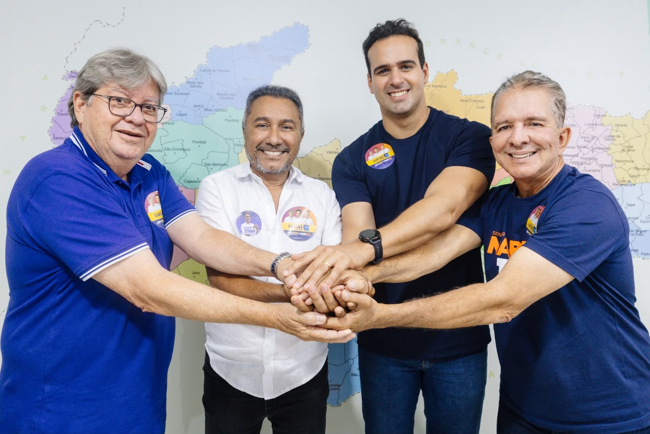 João Azevêdo, Samuka Duarte, Lucas Ribeiro e Nabor Wanderley sorriem e unem as mãos ao centro diante de um mapa da Paraíba na parede.
